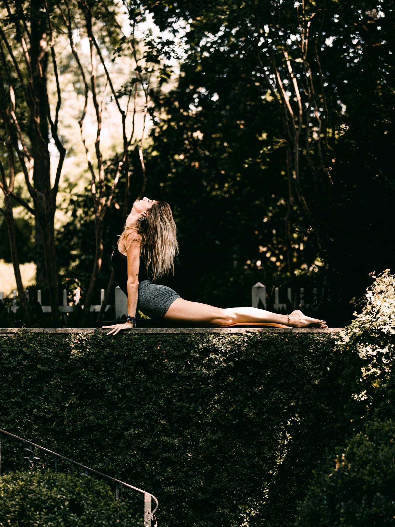 Person in einer Yoga-Rückbeuge auf einer Mauer im Grünen