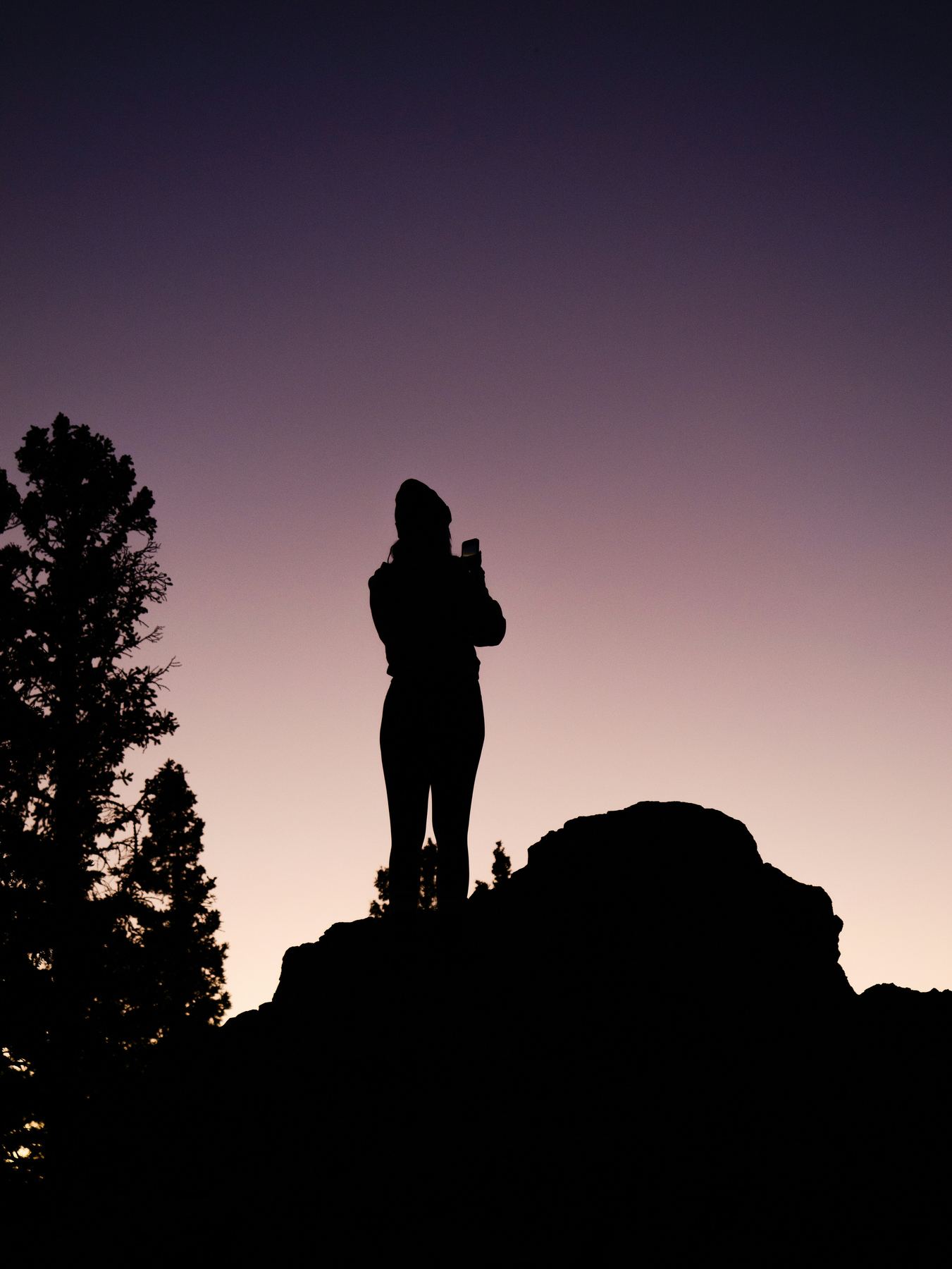 Person steht als Silhouette auf einem Felsen in der Abenddämmerung