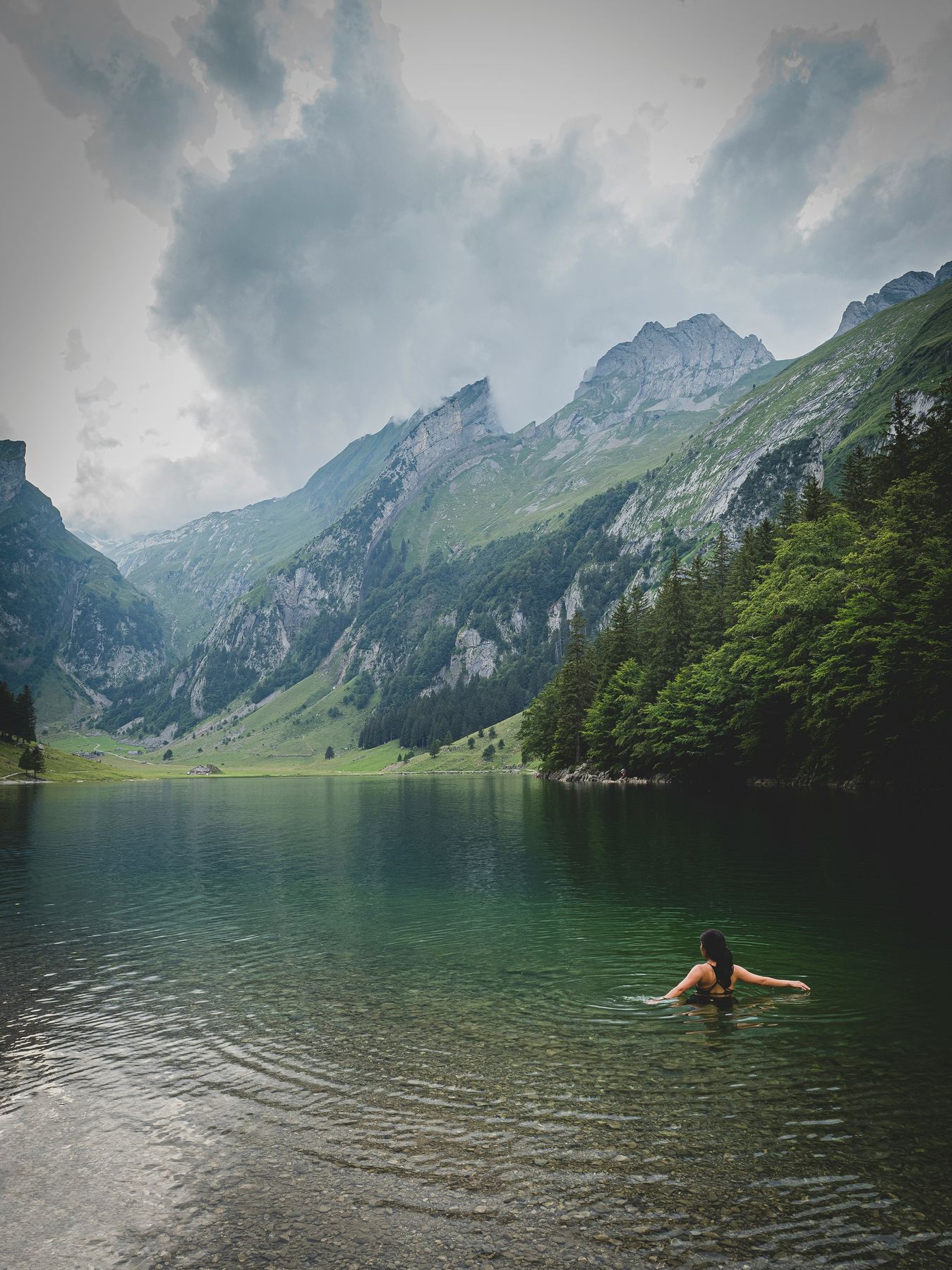 Person schwimmt in einem klaren Bergsee umgeben von Alpen