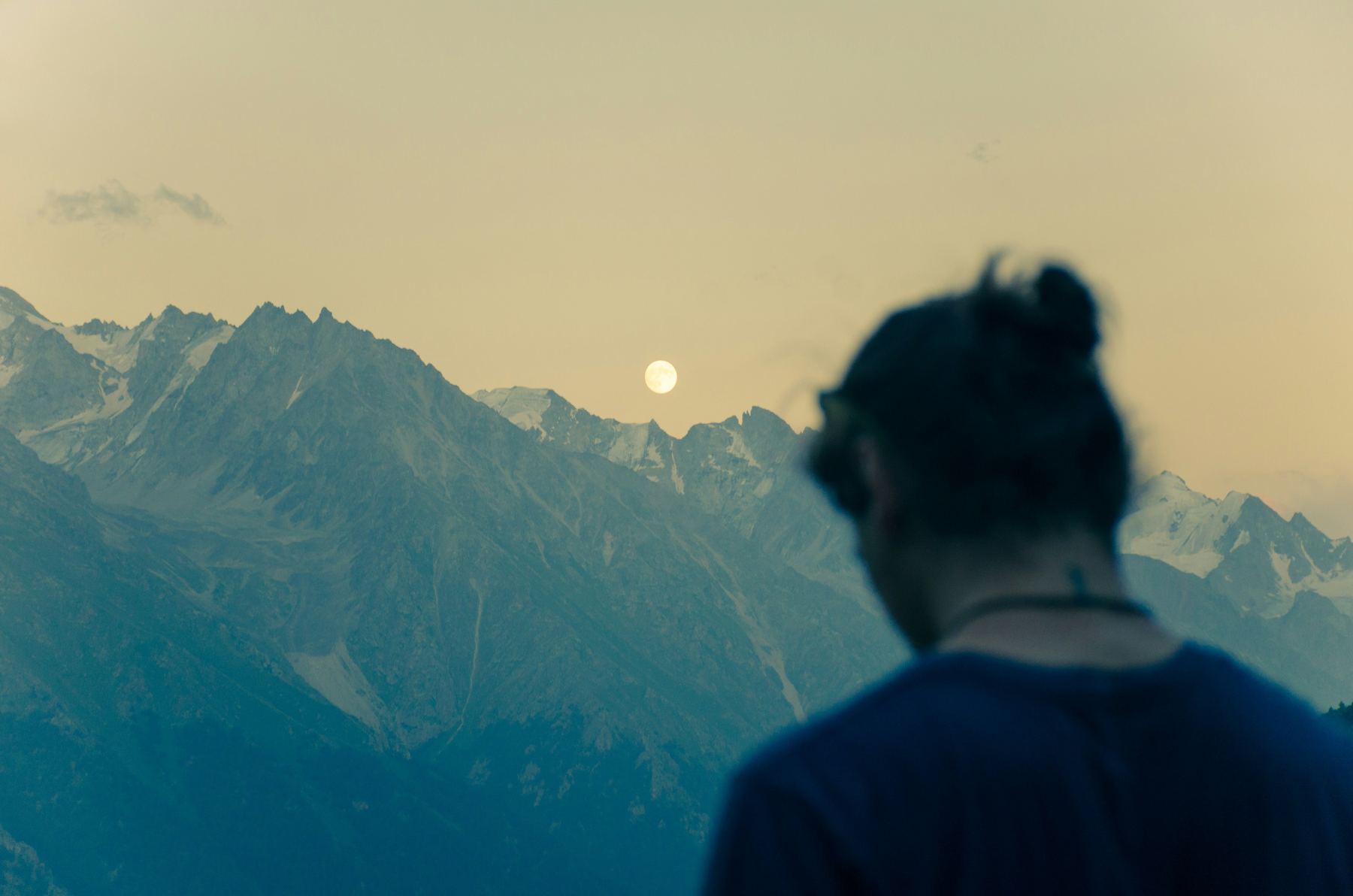 Bergkette bei Sonnenuntergang mit Vollmond, im Vordergrund eine Person von hinten